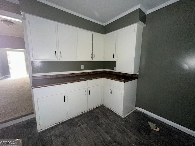 kitchen with dark wood finished floors, crown molding, dark countertops, white cabinets, and baseboards