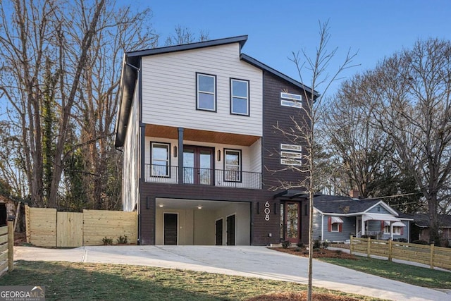 contemporary house with a balcony, driveway, and fence