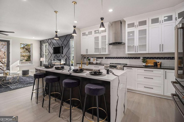 kitchen featuring stainless steel range, light wood-style floors, white cabinetry, wall chimney range hood, and a kitchen breakfast bar