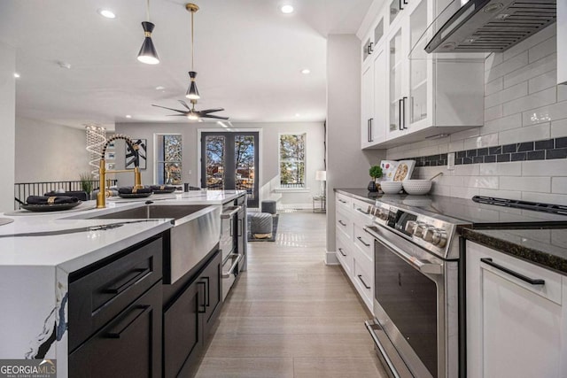 kitchen featuring light wood finished floors, white cabinets, decorative light fixtures, range hood, and stainless steel range with electric stovetop