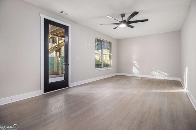 empty room with a ceiling fan, wood finished floors, visible vents, and baseboards