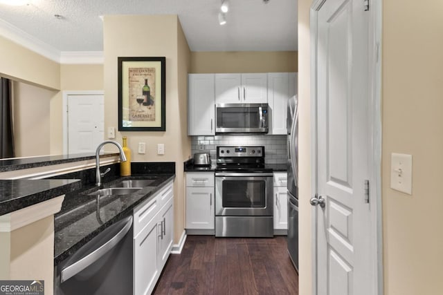 kitchen featuring dark wood-type flooring, a sink, white cabinetry, appliances with stainless steel finishes, and dark stone counters