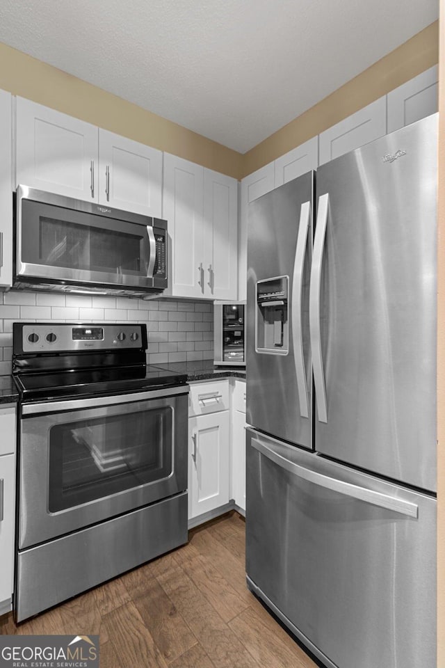 kitchen featuring stainless steel appliances, dark countertops, white cabinetry, and tasteful backsplash