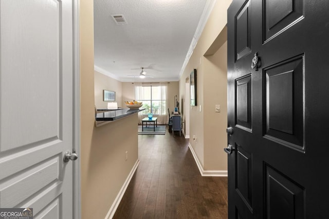 foyer featuring a textured ceiling, dark wood-type flooring, visible vents, baseboards, and crown molding