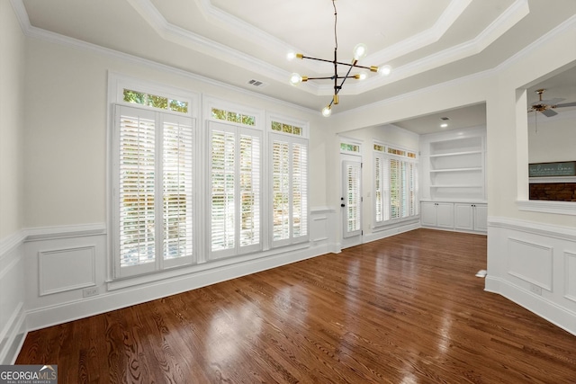 interior space with built in features, a decorative wall, a tray ceiling, and wood finished floors