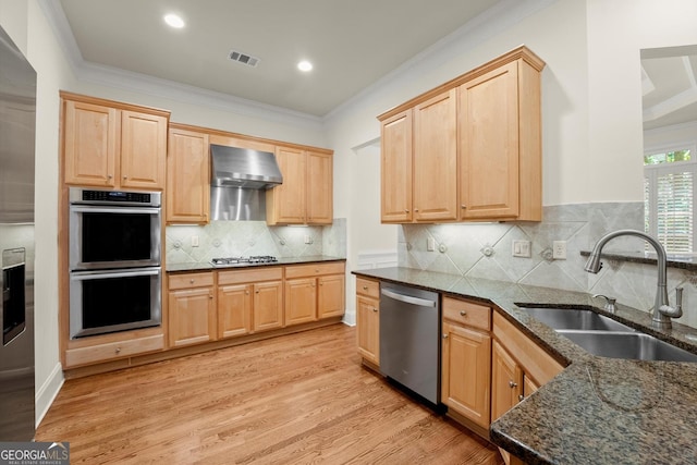 kitchen with visible vents, wall chimney exhaust hood, stainless steel appliances, light brown cabinetry, and a sink