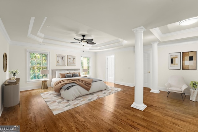 bedroom featuring ornate columns, multiple windows, a tray ceiling, and wood finished floors