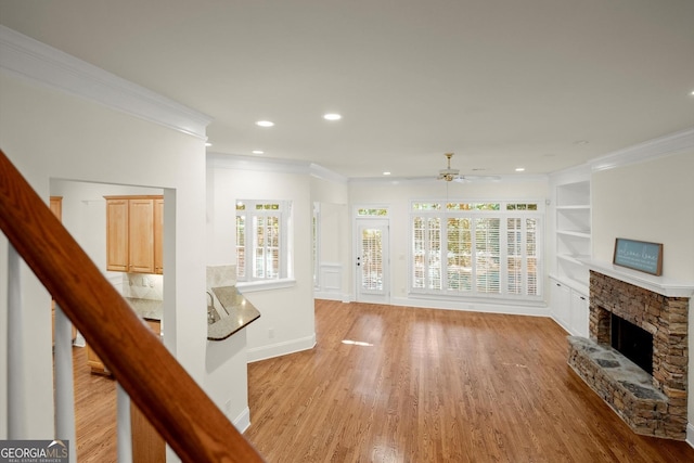 unfurnished living room with light wood-type flooring, built in shelves, a fireplace, and crown molding