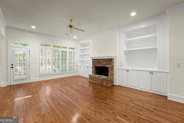 unfurnished living room with baseboards, wood finished floors, crown molding, built in shelves, and a fireplace