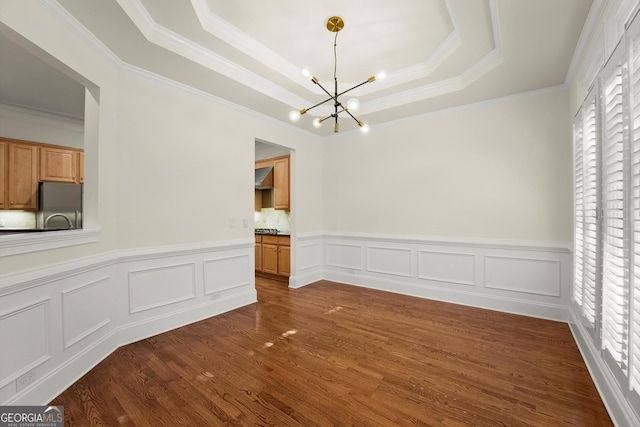 unfurnished dining area with a raised ceiling, ornamental molding, dark wood-style flooring, a decorative wall, and a notable chandelier