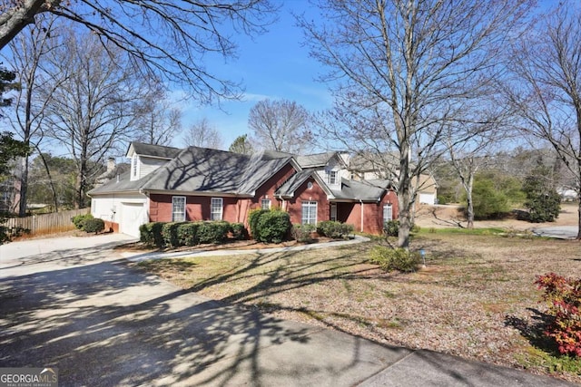 cape cod-style house featuring a garage, concrete driveway, brick siding, and fence