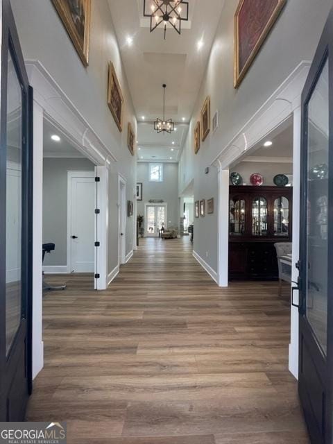 hall featuring baseboards, wood finished floors, a towering ceiling, and a notable chandelier