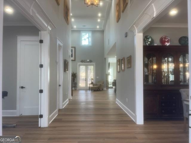 hallway with ornamental molding, a towering ceiling, baseboards, and wood finished floors