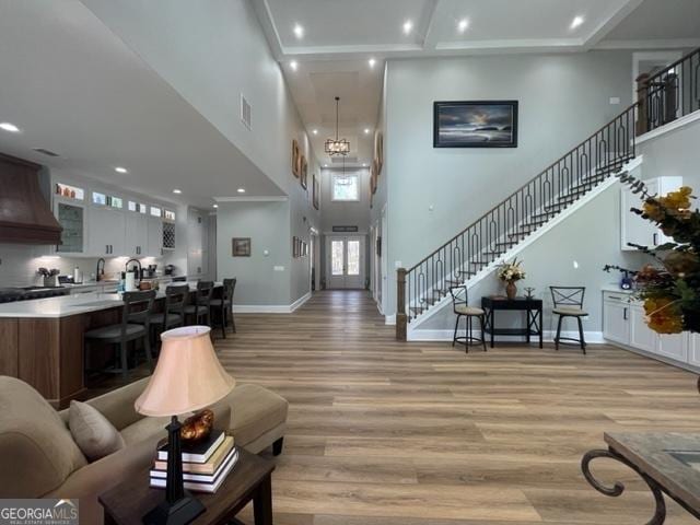 living area featuring stairs, a high ceiling, baseboards, and light wood-style floors