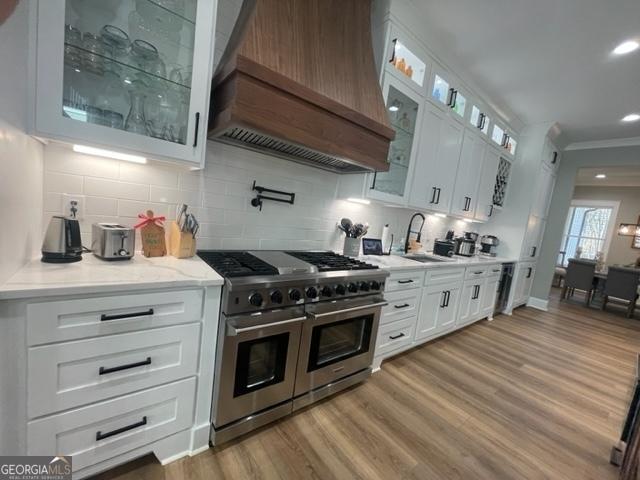 kitchen with range with two ovens, white cabinets, custom range hood, ornamental molding, and light wood-type flooring