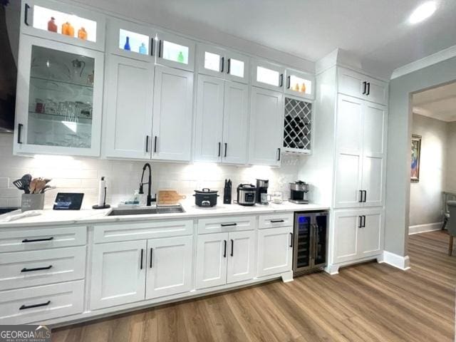 bar with crown molding, tasteful backsplash, light wood-style floors, a sink, and beverage cooler