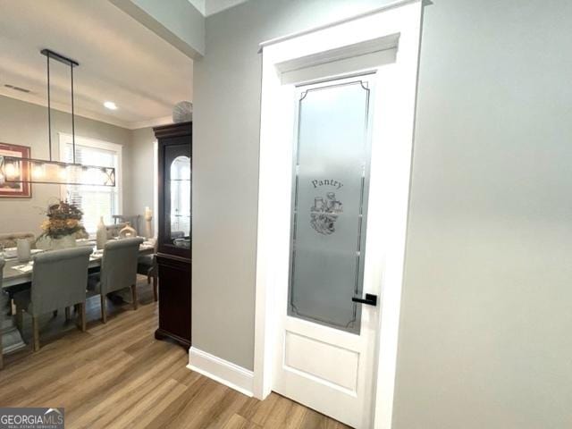 hall featuring baseboards, crown molding, and light wood finished floors