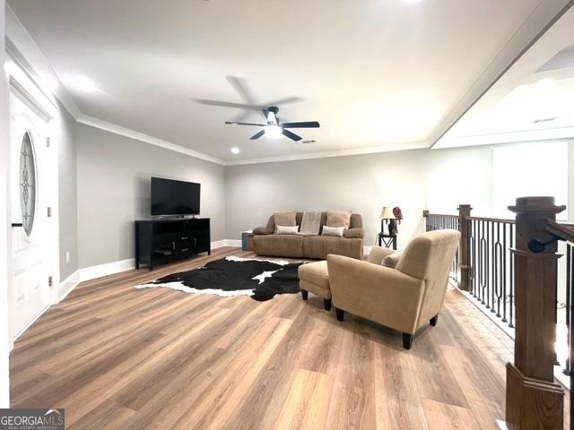 living area featuring baseboards, ceiling fan, wood finished floors, and crown molding