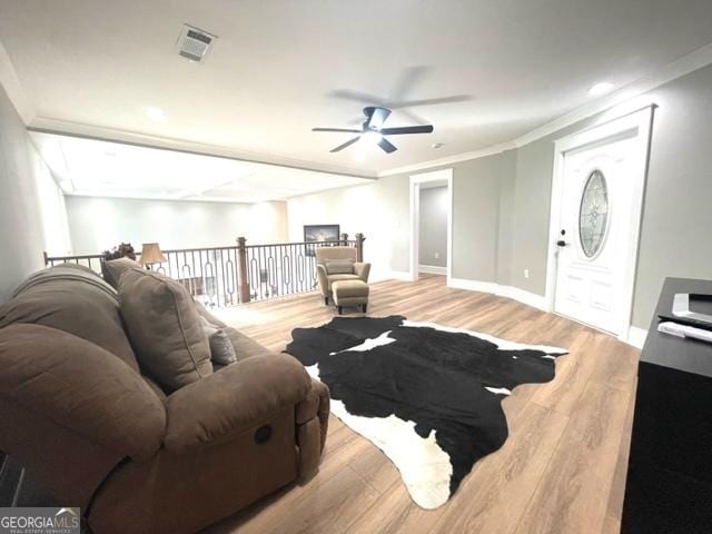 living room featuring baseboards, visible vents, a ceiling fan, wood finished floors, and crown molding