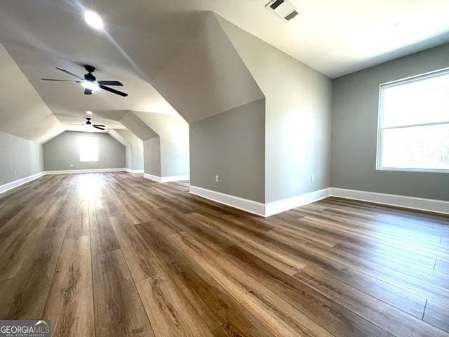 bonus room with dark wood-style floors, lofted ceiling, visible vents, a ceiling fan, and baseboards