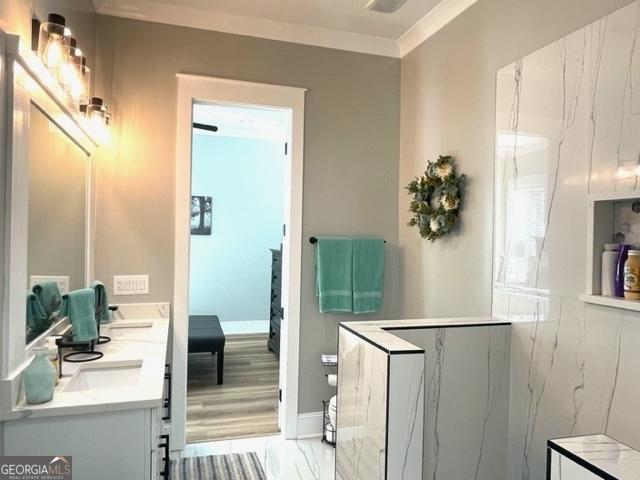 bathroom with marble finish floor, double vanity, baseboards, and crown molding