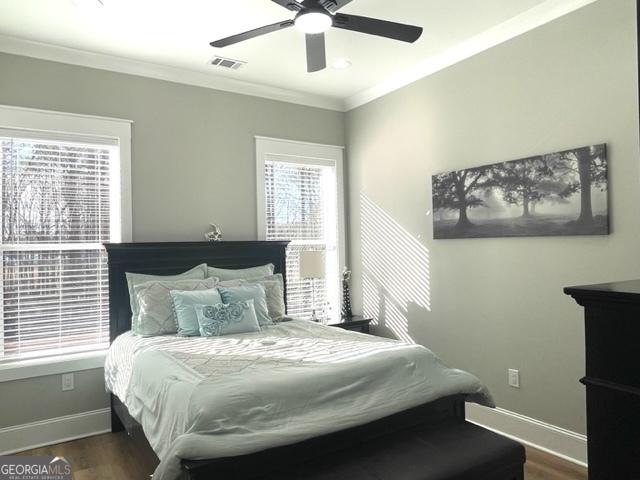 bedroom featuring ceiling fan, wood finished floors, visible vents, baseboards, and ornamental molding