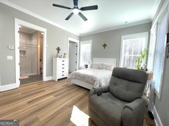 bedroom featuring ensuite bath, baseboards, crown molding, and wood finished floors