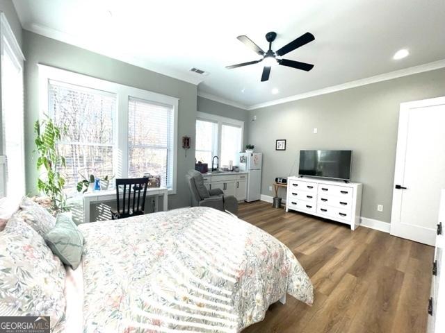 bedroom with ornamental molding, freestanding refrigerator, and wood finished floors