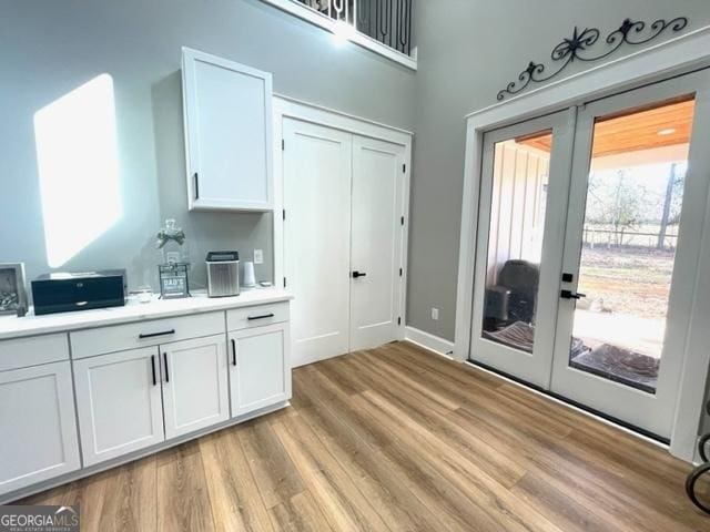 kitchen featuring french doors, light wood finished floors, light countertops, a high ceiling, and white cabinetry