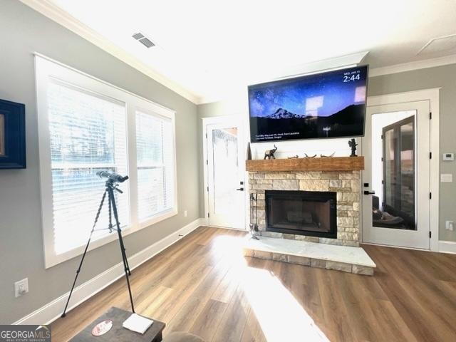 unfurnished living room featuring wood finished floors, crown molding, and a stone fireplace