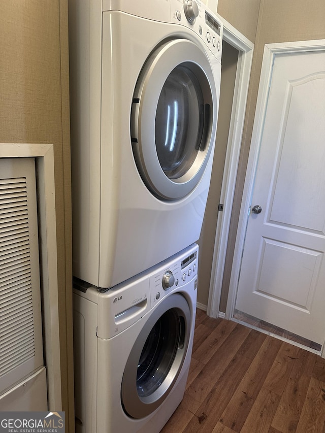 clothes washing area featuring stacked washer / dryer, laundry area, a heating unit, and wood finished floors