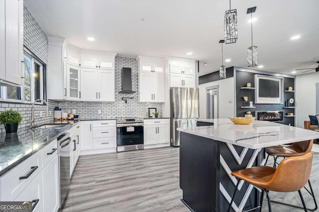 kitchen featuring decorative backsplash, appliances with stainless steel finishes, glass insert cabinets, a sink, and wall chimney range hood