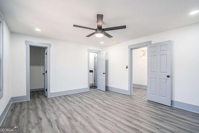 unfurnished bedroom featuring ceiling fan, recessed lighting, wood finished floors, baseboards, and a walk in closet