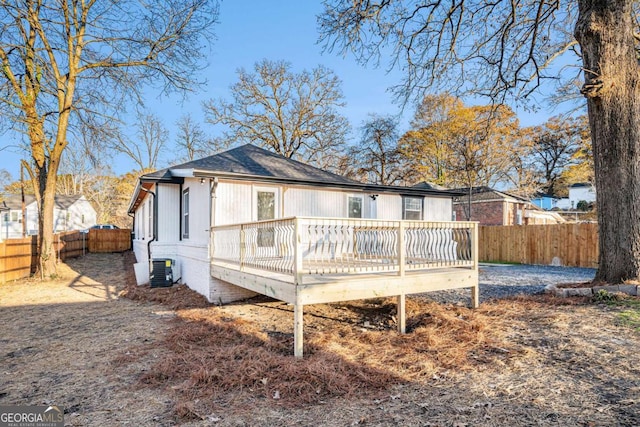 rear view of property featuring a fenced backyard, central AC unit, a deck, and roof with shingles