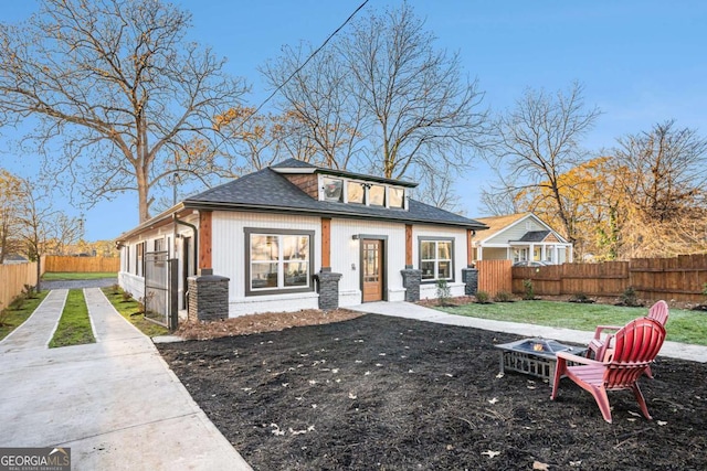 back of property with a fire pit, a shingled roof, and fence