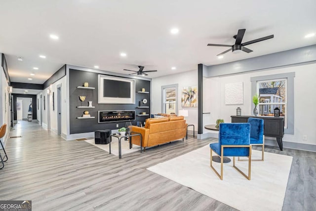 living area with recessed lighting, a glass covered fireplace, ceiling fan, wood finished floors, and baseboards