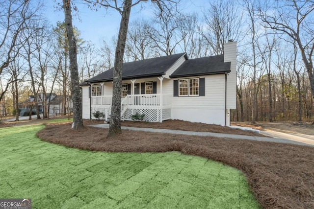 single story home featuring a porch, a chimney, and a front yard