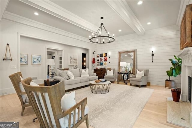 living room with light wood-style flooring, an inviting chandelier, ornamental molding, a high end fireplace, and beamed ceiling