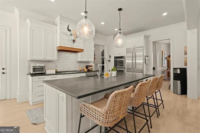 kitchen featuring tasteful backsplash, dark countertops, light wood-style flooring, stainless steel appliances, and a sink