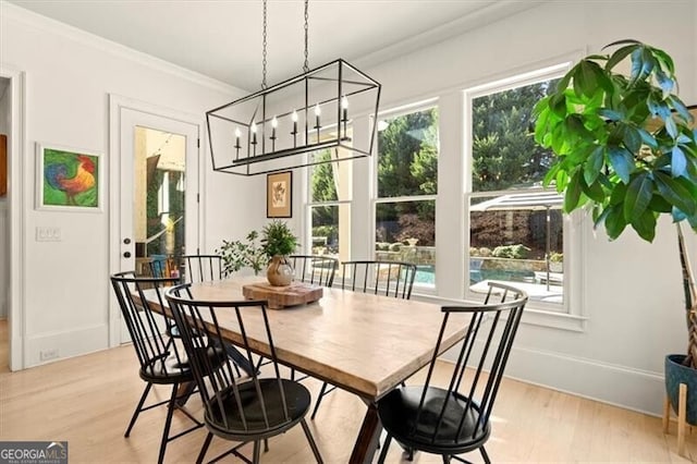 dining room featuring light wood-type flooring, a notable chandelier, baseboards, and crown molding