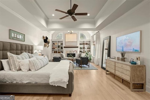 bedroom featuring a tray ceiling, crown molding, light wood-style floors, a fireplace, and recessed lighting