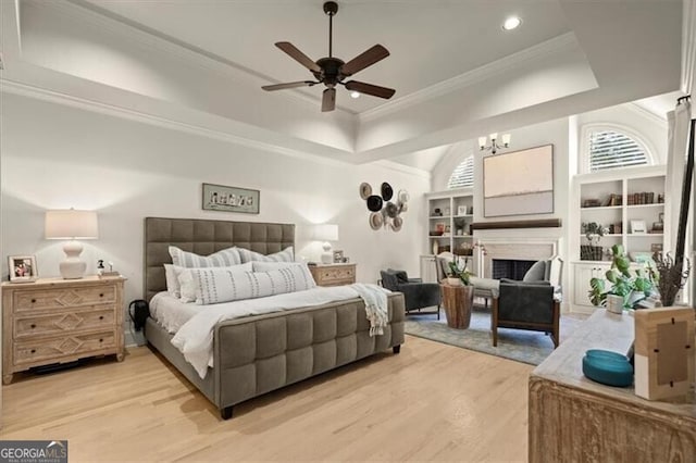 bedroom featuring light wood-type flooring, a fireplace, a tray ceiling, and ornamental molding