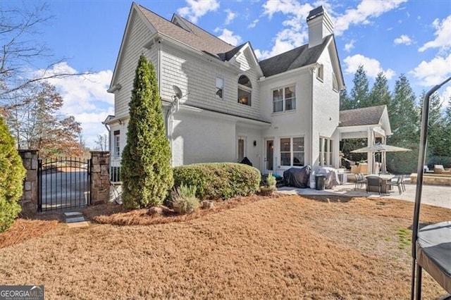 rear view of property with a patio, a chimney, and a gate