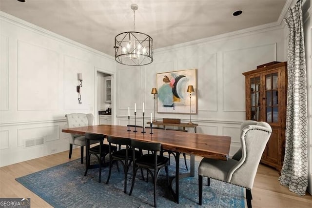 dining room featuring light wood-type flooring, visible vents, ornamental molding, and a decorative wall