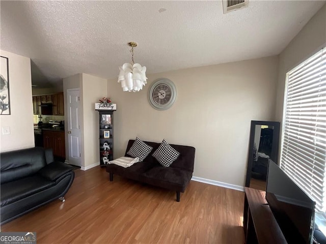 living room featuring light wood-type flooring, visible vents, a chandelier, and a textured ceiling