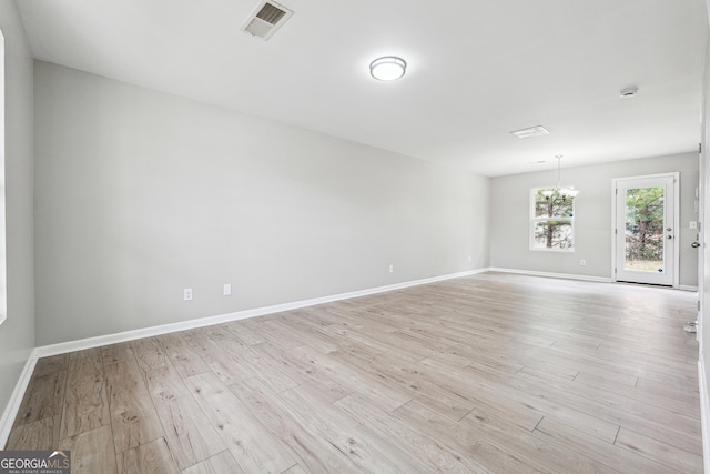 spare room with light wood finished floors, baseboards, visible vents, and a notable chandelier