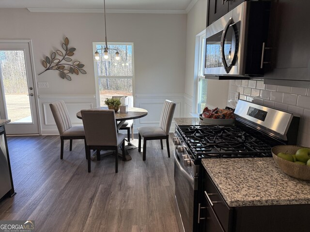 kitchen featuring dark cabinets, a wainscoted wall, dark wood-style flooring, ornamental molding, and appliances with stainless steel finishes