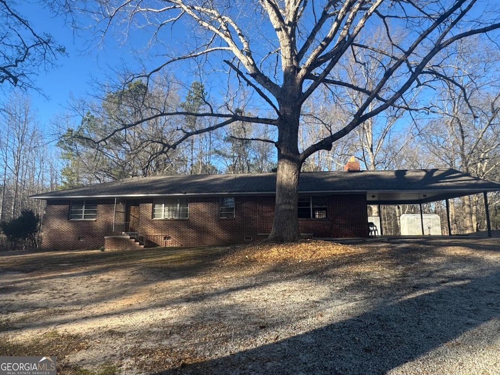 view of property exterior with driveway, a chimney, an attached carport, crawl space, and brick siding