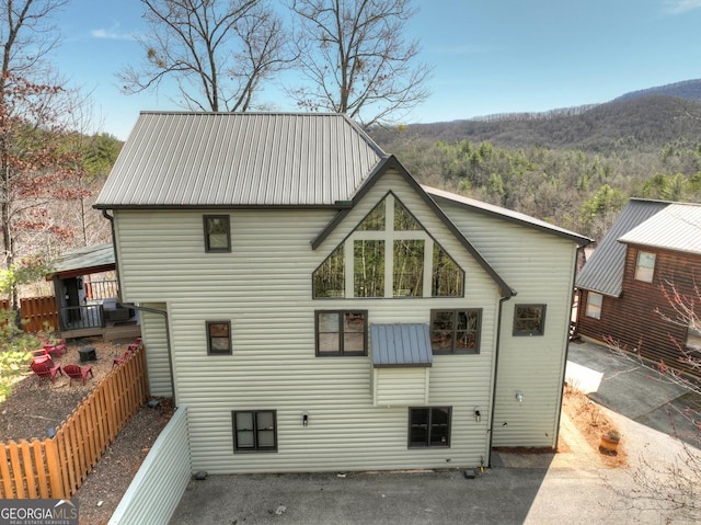 back of property with a mountain view, fence, and metal roof