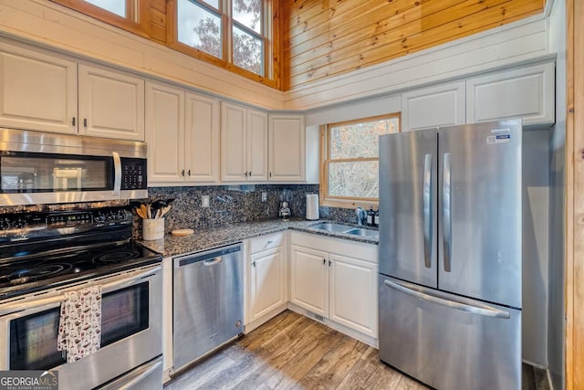 kitchen with light wood-style flooring, stainless steel appliances, a sink, white cabinetry, and dark stone counters